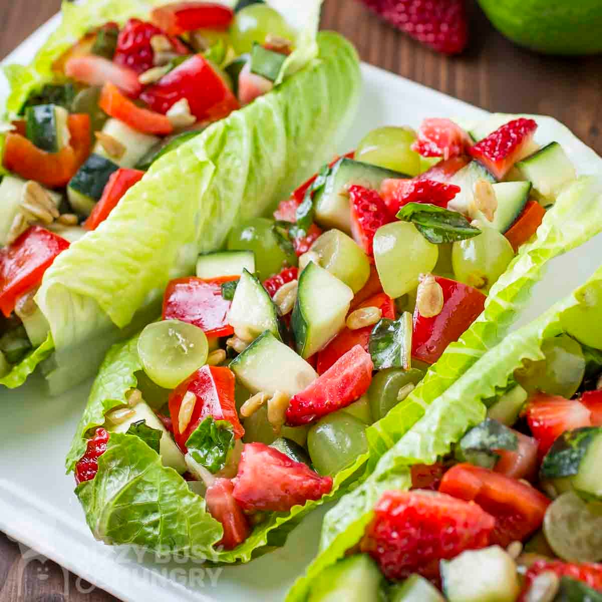 Side close up shot of three lettuce boats filled with fruit and veggie salad on a white plate.