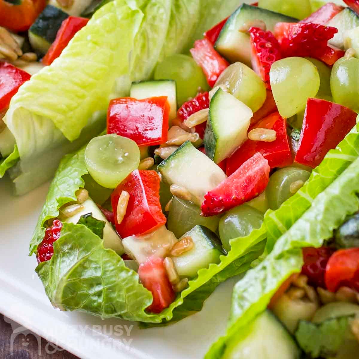 Side close up shot of three lettuce boats filled with fruit and veggie salad on a white plate.