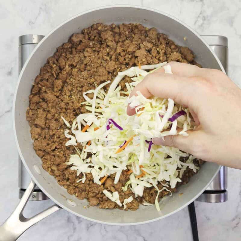 Overhead view of process shot 4 - add the coleslaw mix into the skillet and stir together with the turkey.