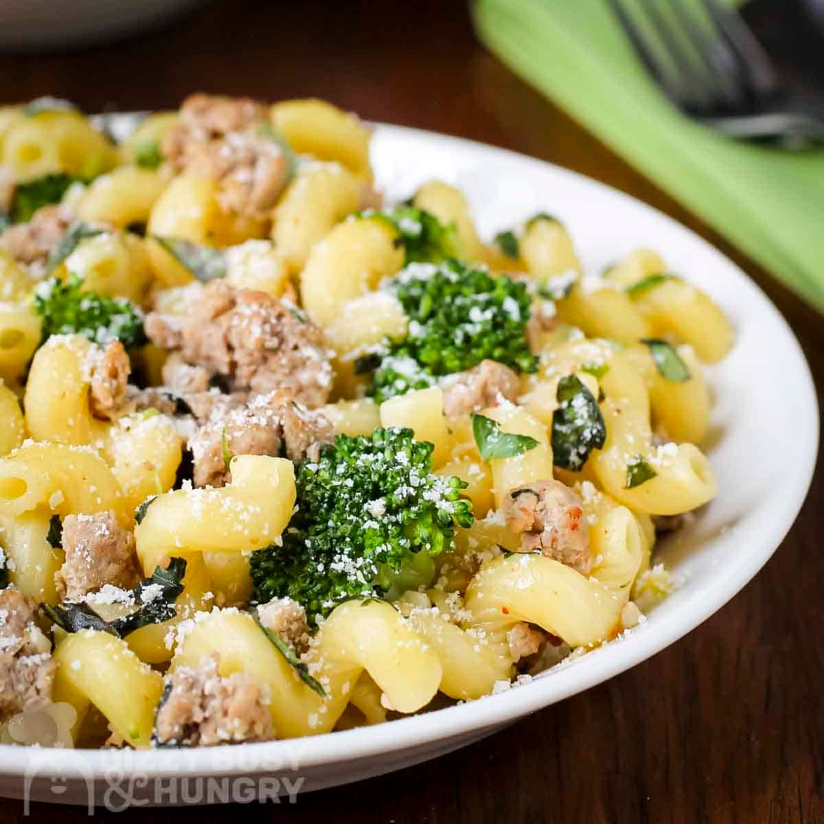 Side shot of turkey and broccoli pasta sprinkled wiith parmesan cheese in a white bowl with a fork and green cloth on the side.