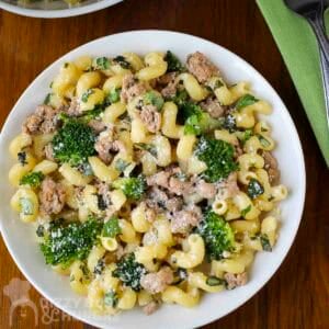 Overhead shot of turkey and broccoli pasta sprinkled wiith parmesan cheese in a white bowl with a fork and green cloth on the side.