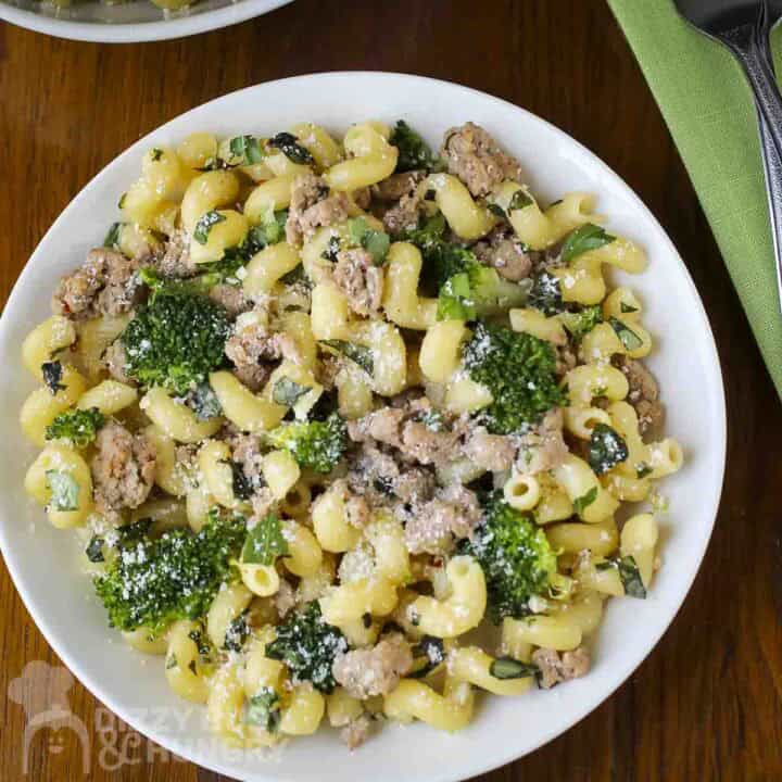 Overhead shot of turkey and broccoli pasta sprinkled wiith parmesan cheese in a white bowl with a fork and green cloth on the side.