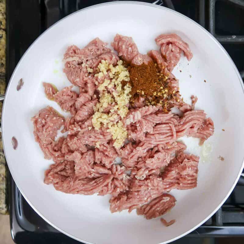 Overhead view of process shot 2 - heat one tablespoon of olive oil over medium high heat. Add the turkey, paprika, garlic, red pepper flakes, and salt.