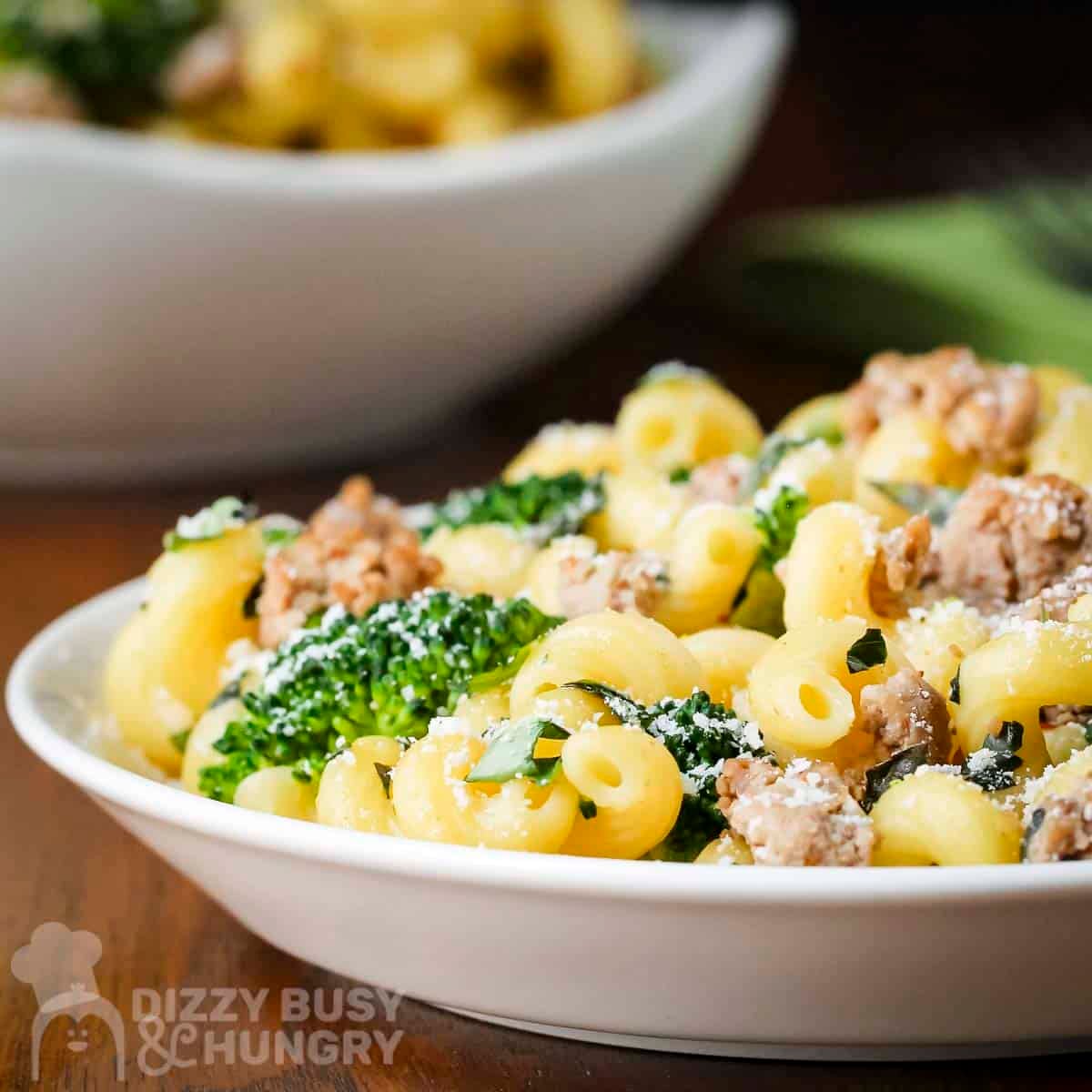 Side shot of turkey and broccoli pasta sprinkled wiith parmesan cheese in a white bowl with a fork and green cloth on the side.