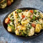 Side shot of two plates of pesto chicken and gnocchi sprinkled with shredded parmesan on black plates.