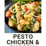 Side shot of pesto chicken and gnocchi sprinkled with shredded parmesan on a black plate.