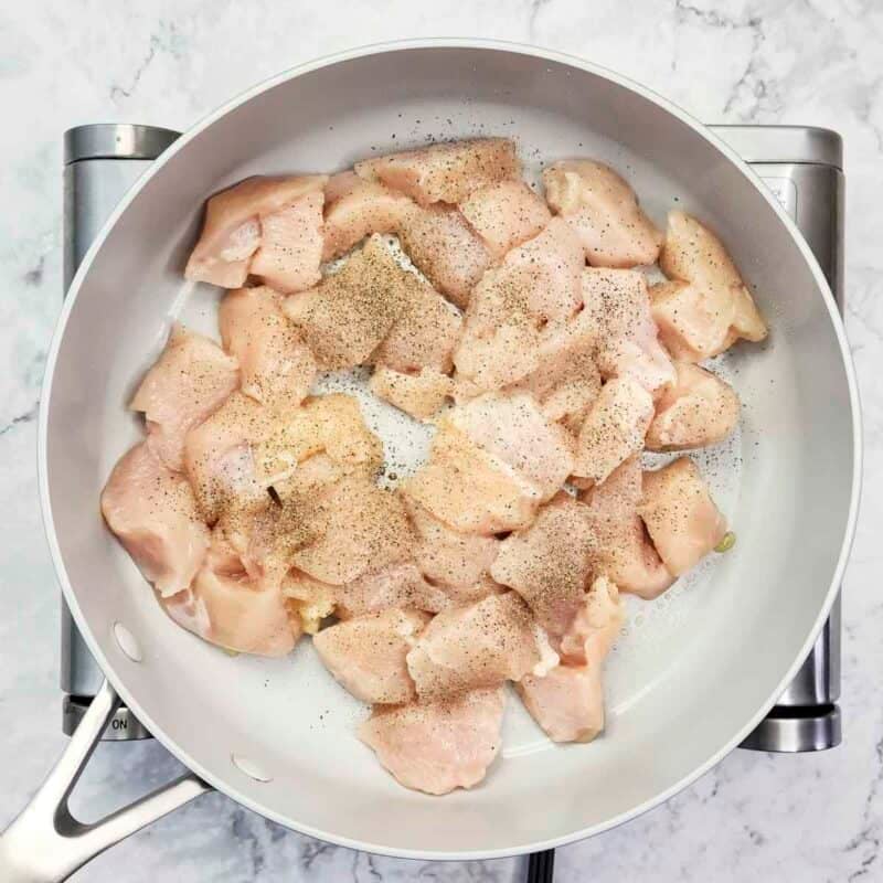 Overhead view of process shot 1 - heat the olive oil in a large skillet over medium-high heat. Add the chicken pieces to the skillet, season with salt and pepper, and cook about 5-7 minutes until the chicken is cooked through.