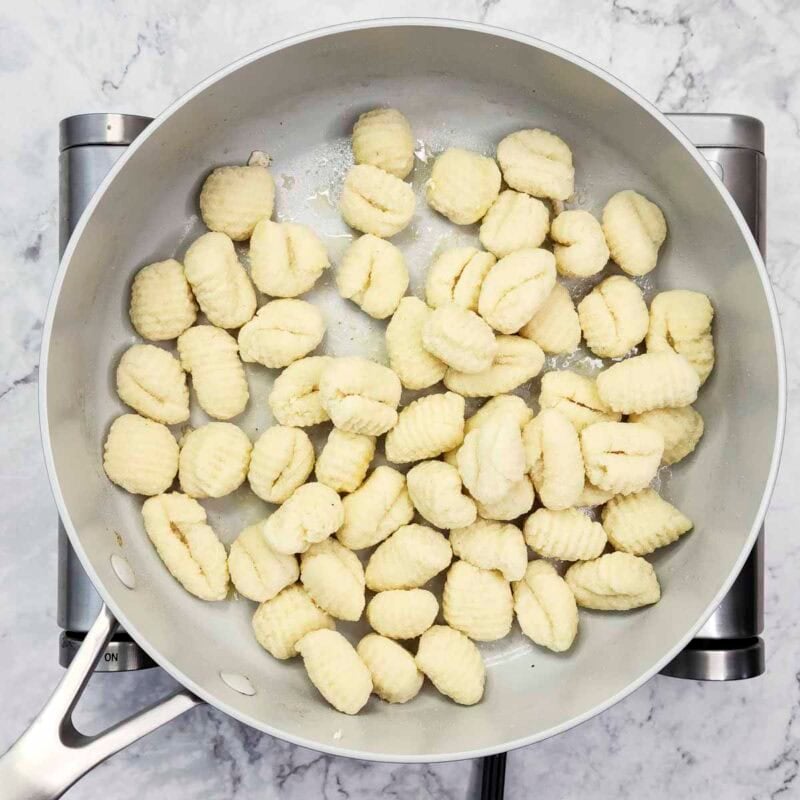 Overhead view of process shot 2 - add the gnocchi to the skillet. Let them sit undisturbed for 2-3 minutes until the bottoms are golden brown, then stir and cook for another 2 minutes.