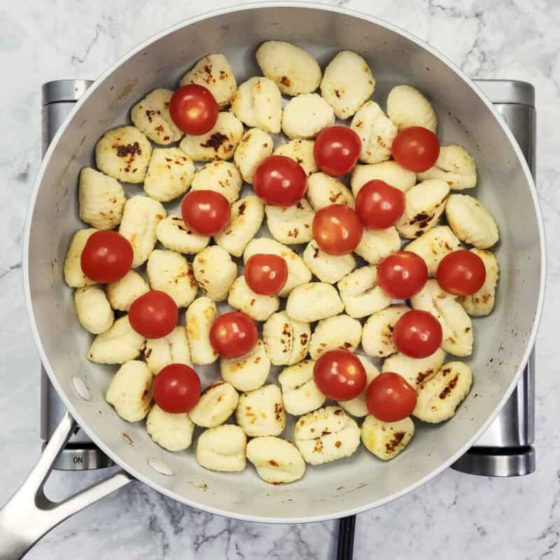 Overhead view of process shot 3 - add the cherry tomatoes to the pan with the gnocchi. Cover with lid, reduce the heat, and cook for 2-4 minutes, until the gnocchi get steamed through and the tomatoes start to split.
