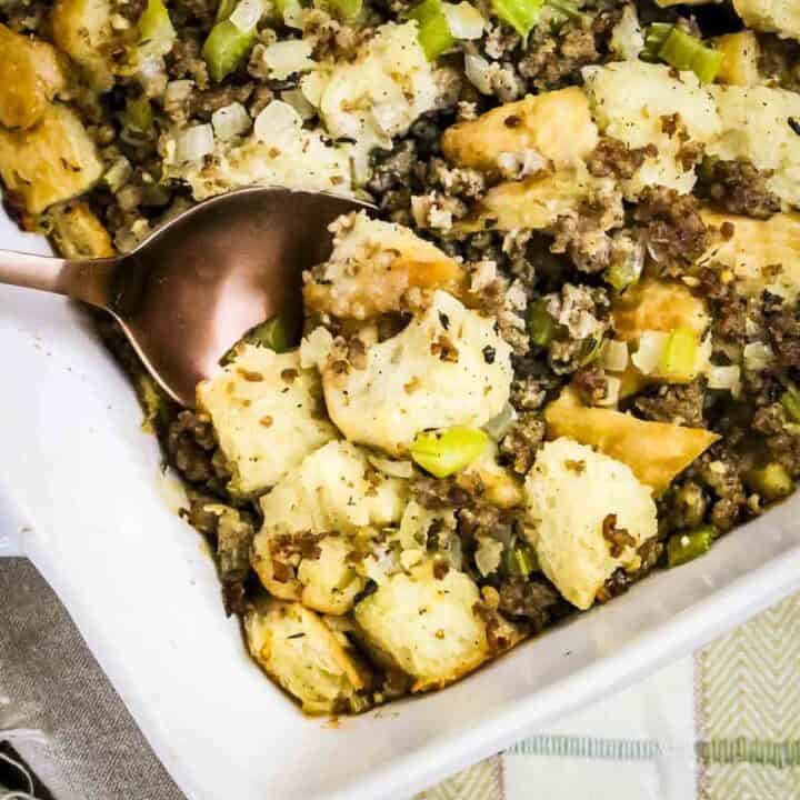 Close up shot of sage and sausage stuffing in a white baking dish with a spoon taking a scoop out.