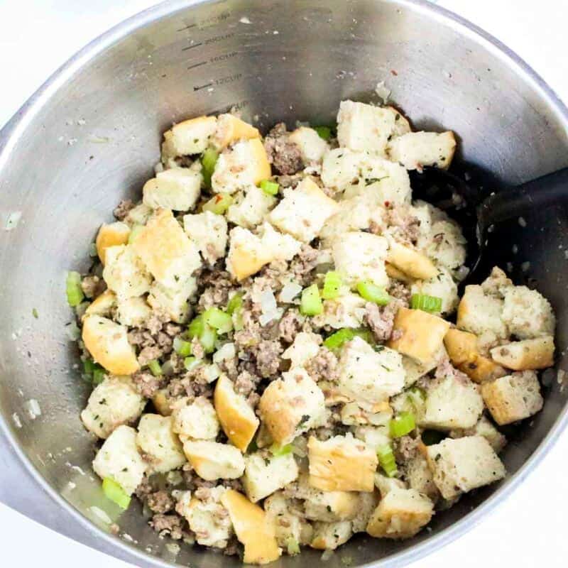 Overhead view of process shot 3 - in a large mixing bowl, combine the bread cubes, sausage, and sauteed vegetables. Stir in the chicken broth and melted butter until evenly moistened.