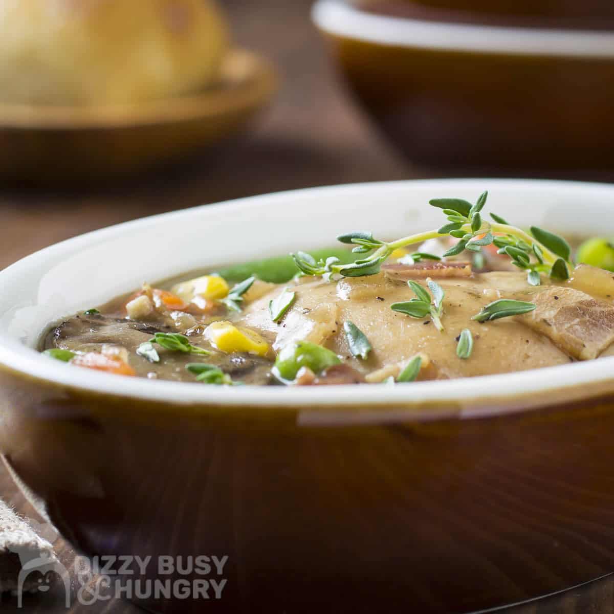 Side shot of chicken stew garnished with fresh thyme in a white oval bowl on a wooden surface.