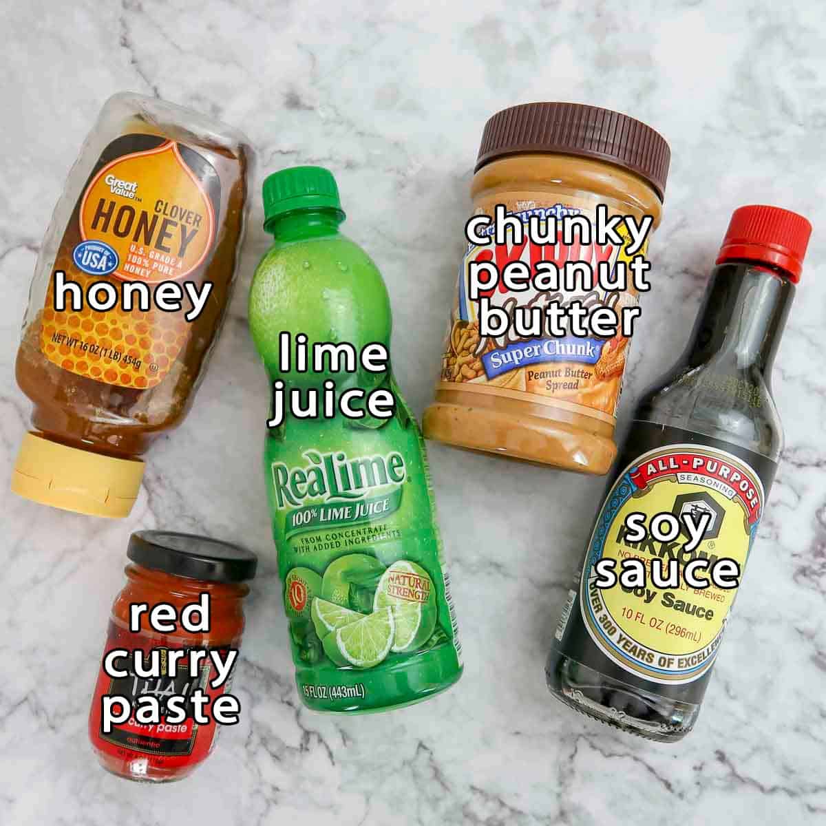 Overhead shot of peanut sauce ingredients - honey, red curry paste, lime juice, chunky peanut butter, and soy sauce.