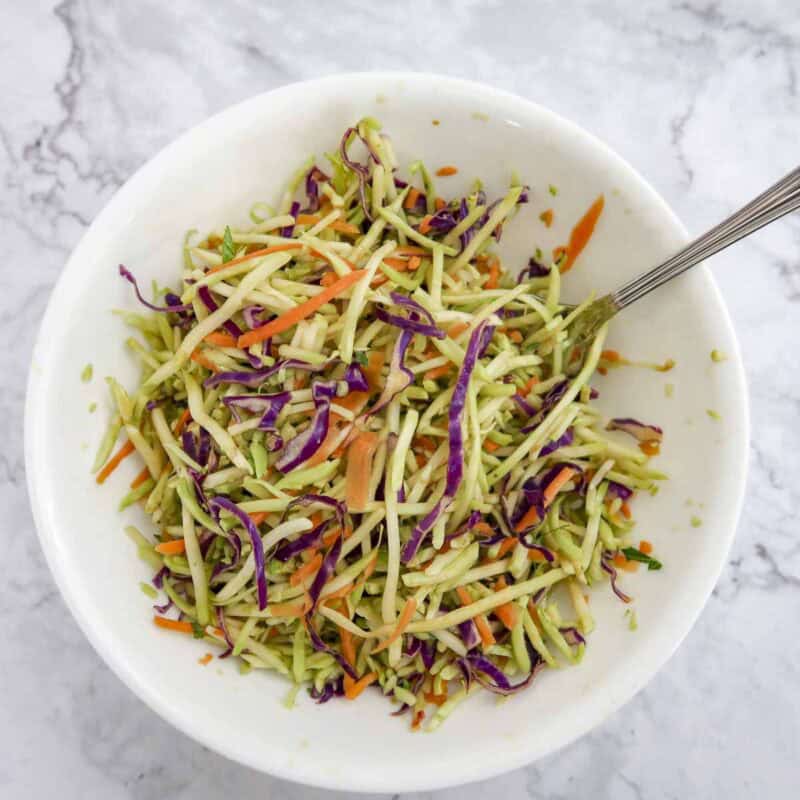 Overhead view of slaw process shot 1 - combine the broccoli slaw, lime juice, rice wine vinegar, and soy sauce in a medium bowl to make the slaw.