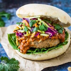 Side close up shot of thai turkey burger garnished with fresh parsley on a piece of brown parchment paper.