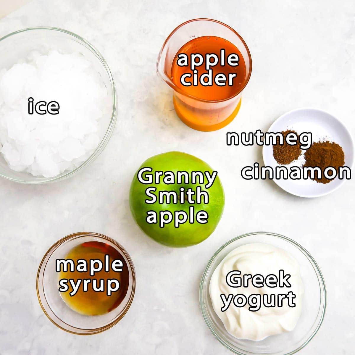 Overhead view of ingredients - ice, apple cider, granny smith apple, maple syrup, greek yogurt, nutmeg, and cinnamon.