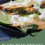 Side shot of multiple bean and cheese quesadillas garnished with fresh herbs and crema on a black plate with a lime wedge on the side.