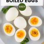 Overhead view of multiple peeled boiled eggs, some cut in half, on a white plate with fresh herbs on the side.