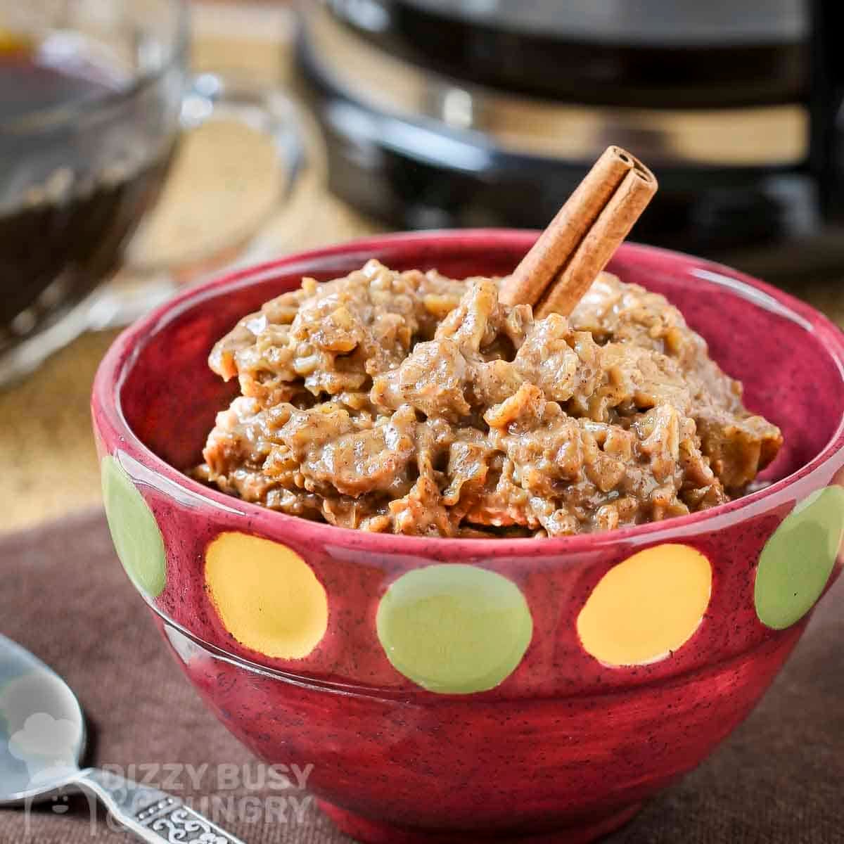 Side shot of instant coffee oatmeal with two cinnamon sticks in a red bowl with yellow and green polka dots.