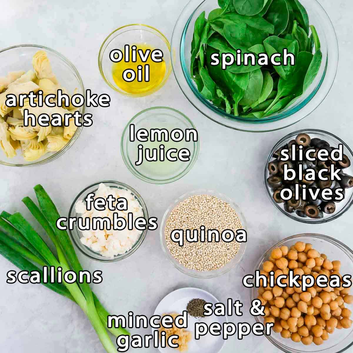 Overhead shot of ingredients - spinach, olive oil, artichoke hearts, lemon juice, sliced black olives, feta crumbles, quinoa, chickpeas, scallions, minced garlic, salt, and pepper.