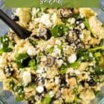 Overhead shot of quinoa salad in a glass bowl with a black spoon on a blue surface.
