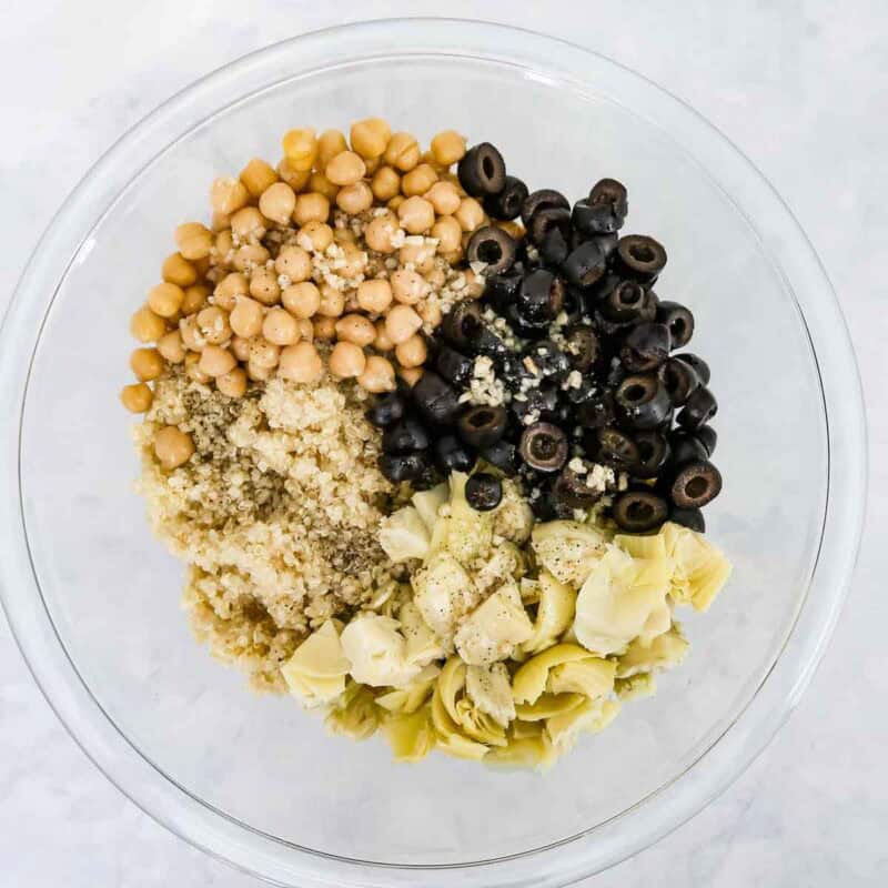 Overhead view of process shot 3 - when the quinoa is done, let it sit for about 10 minutes to cool slightly, then add the olive oil/lime juice mixture, chickpeas, black olives, and artichoke hearts, and mix together.