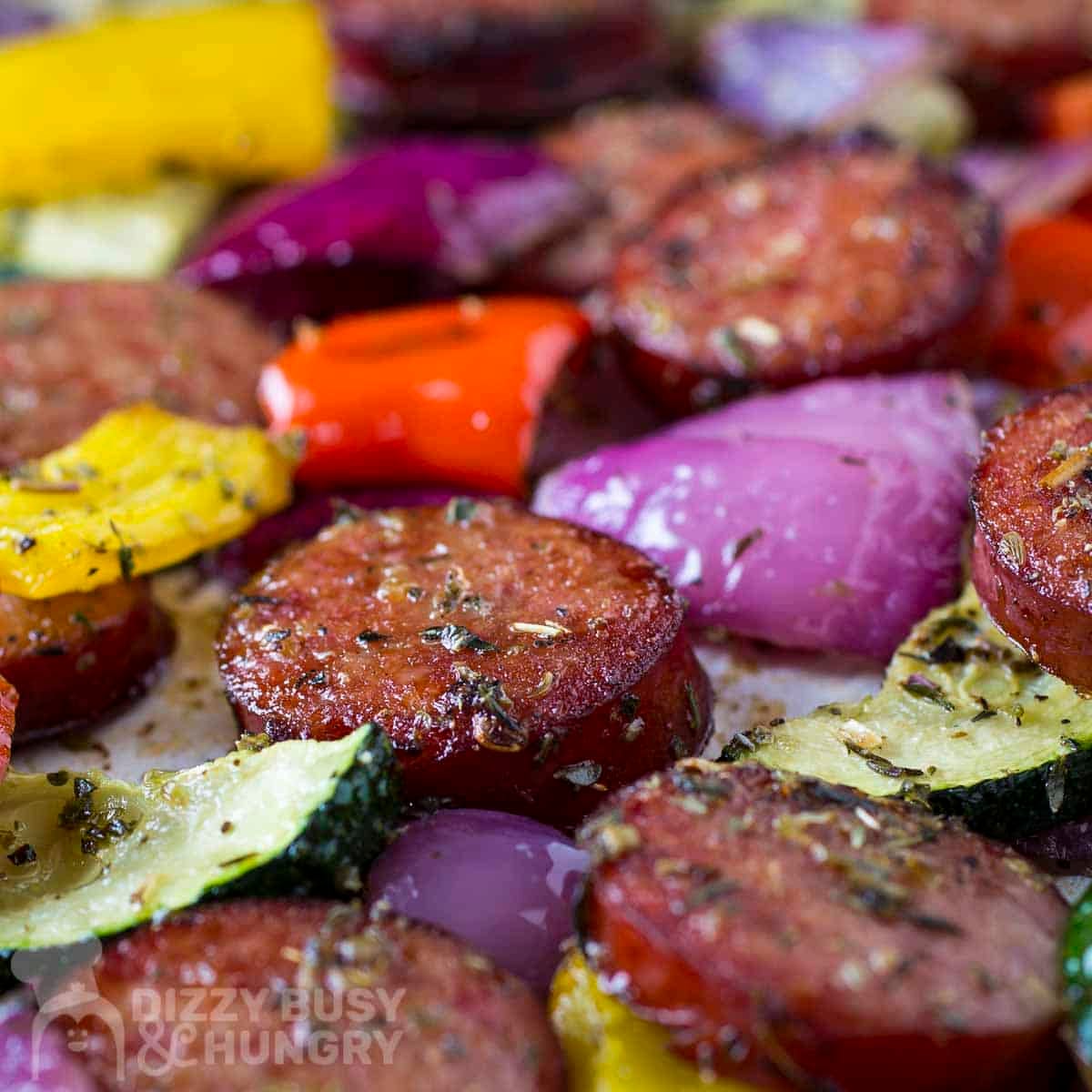 Close up view of kielbasa and veggies on a parchment paper-lined baking sheet.