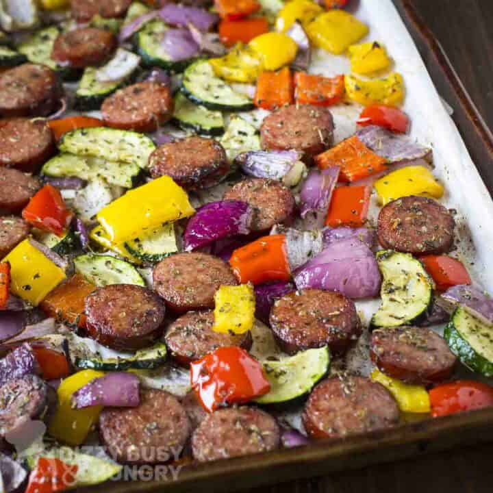 Close up angled view of kielbasa and veggies on a parchment paper-lined baking sheet.