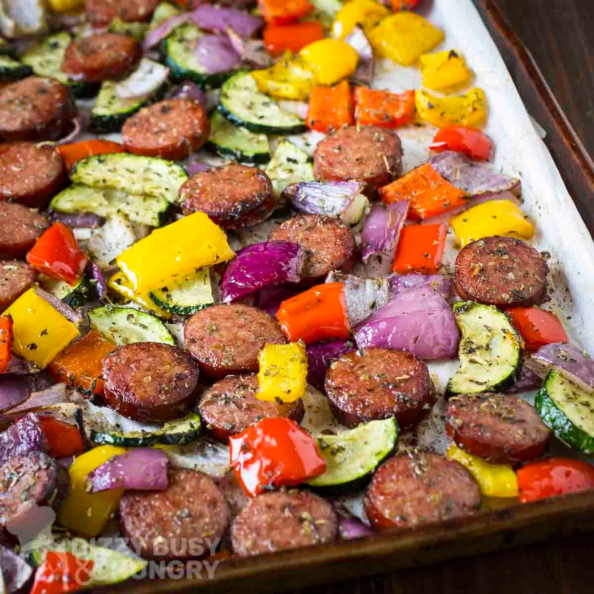 Close up angled view of kielbasa and veggies on a parchment paper-lined baking sheet.