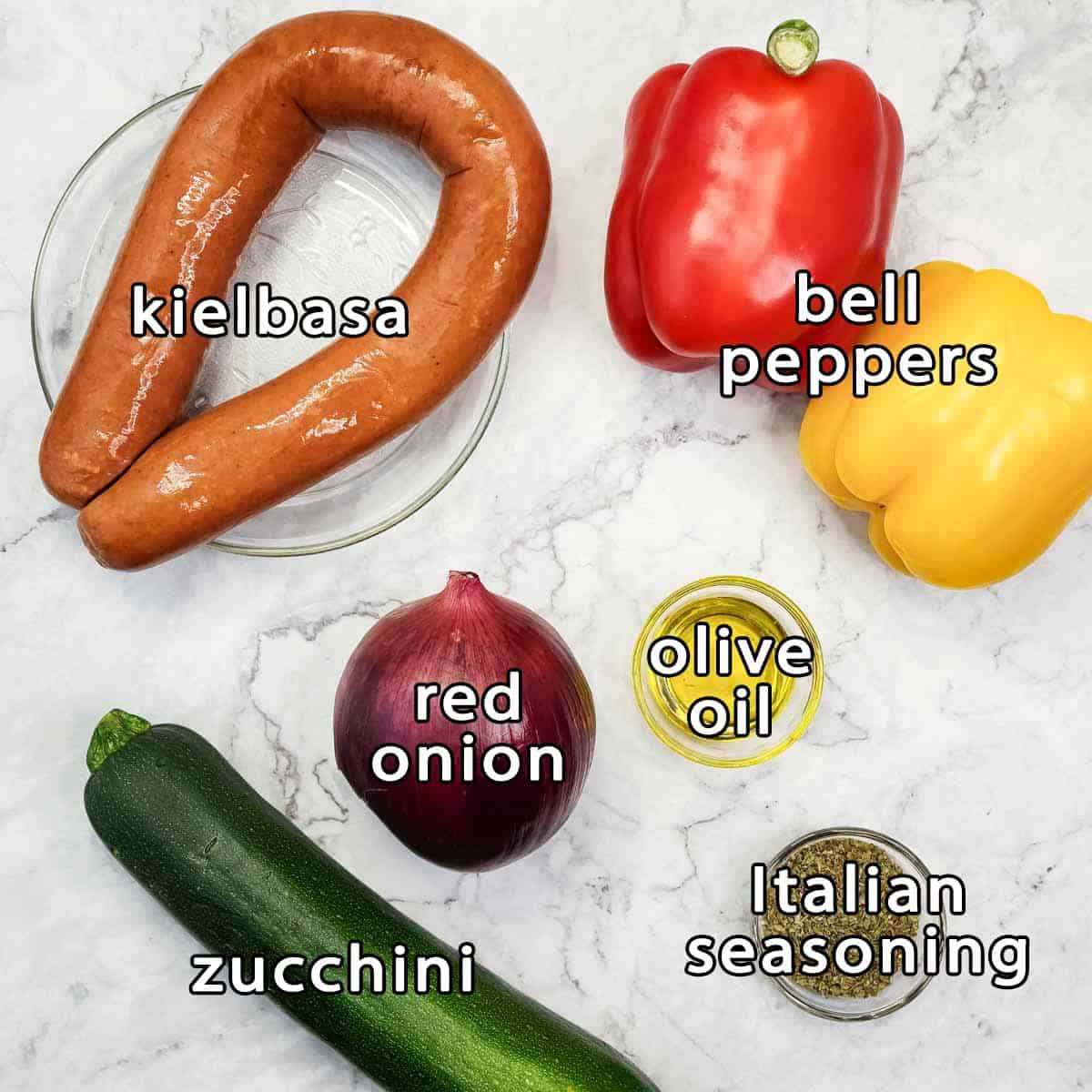 Overhead shot of ingredients - kielbasa, bell peppers, red onion, zucchini, olive oil, and italian seasoning.