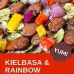 Close up overhead view of kielbasa and veggies on a parchment paper-lined baking sheet.