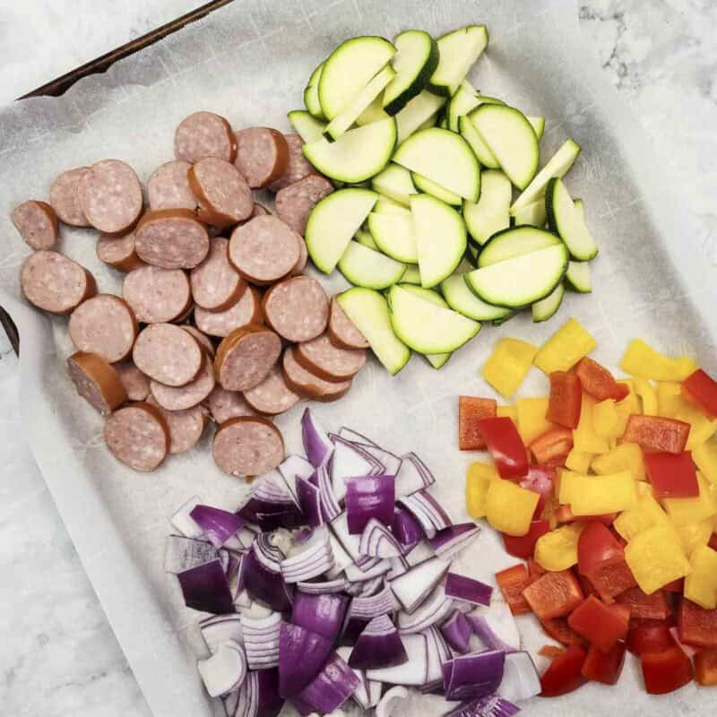 Overhead view of process shot 1 - chop the kielbasa and each of the veggies into bite-sized pieces. Arrange on a parchment-paper lined baking sheet.