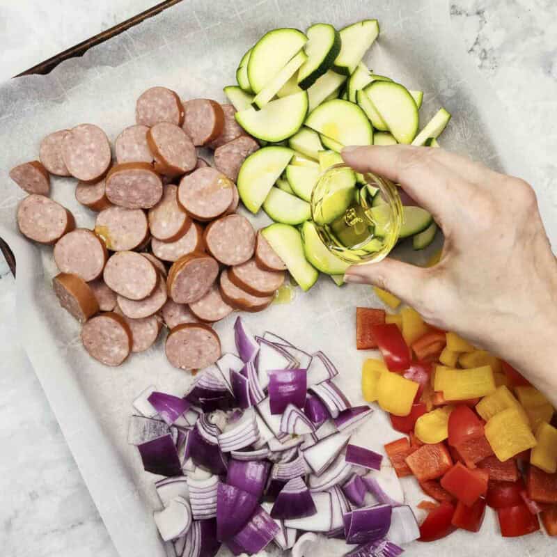 Overhead view of process shot 2 - drizzle the olive oil evenly across the kielbasa and veggies.