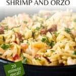 Side close up shot of shrimp and orzo garnished with fresh herbs in a cast iron skillet on a blue surface.