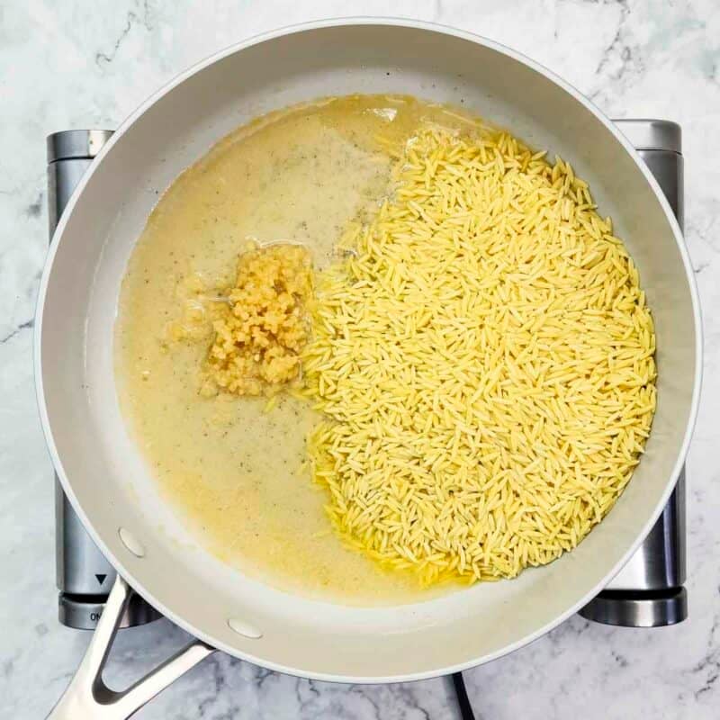 Overhead view of process shot 2 - in the same pan, add the minced garlic and the dry orzo.