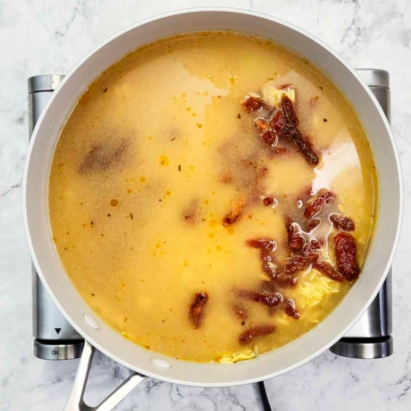 Overhead view of proces shot 3 - pour in the broth and the sun-dried tomatoes. Bring to a boil, then turn the heat down to low. Cover and simmer for 8-10 minutes.
