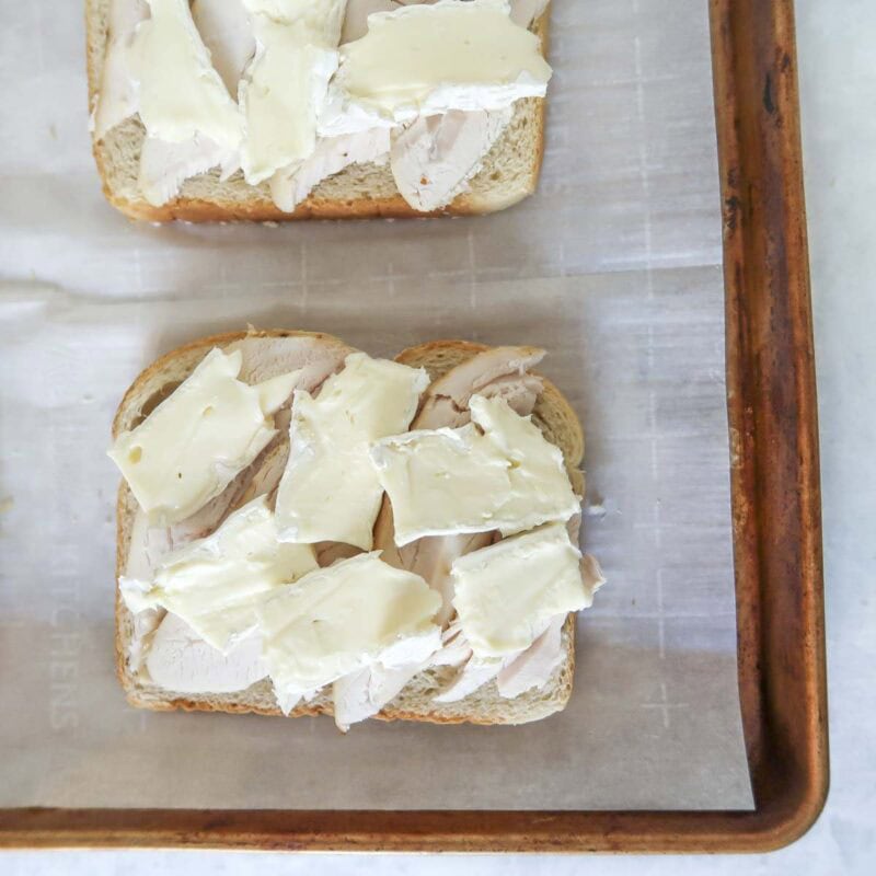 Overhead view of process shot 3 - butter one side of 4 slices of bread with the butter and place them butter side down on a baking sheet. Distribute the turkey across the 4 slices, then distribute the brie.