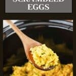 Side shot of a wooden spoon holding a scoop of eggs over a black crockpot bowl with scrambled eggs garnished with fresh herbs.