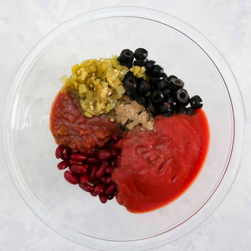 Overhead view of process shot 1 - combine the salsa, tomato sauce, chiles, kidney beans, olives, and cumin in a large bowl.
