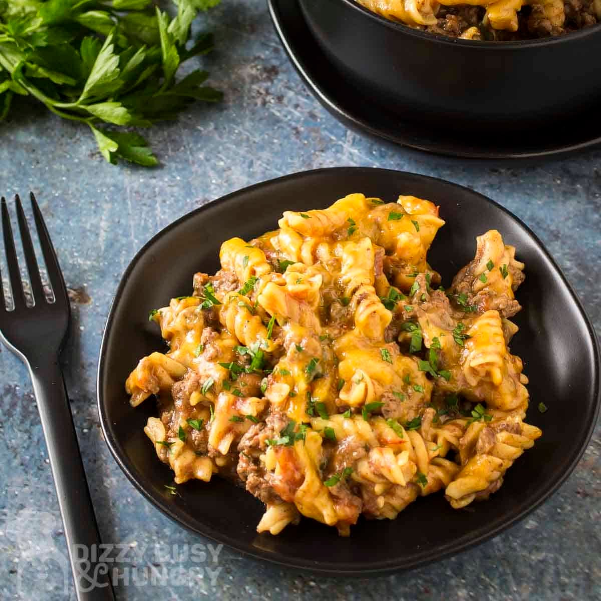 Side angled shot of taco pasta garnished with fresh herbs on a black plate with a black fork and herbs on the side.