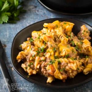 Side angled shot of taco pasta on a black plate garnished with fresh herbs with more herbs in the background.