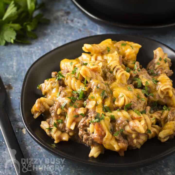Side angled shot of taco pasta on a black plate garnished with fresh herbs with more herbs in the background.