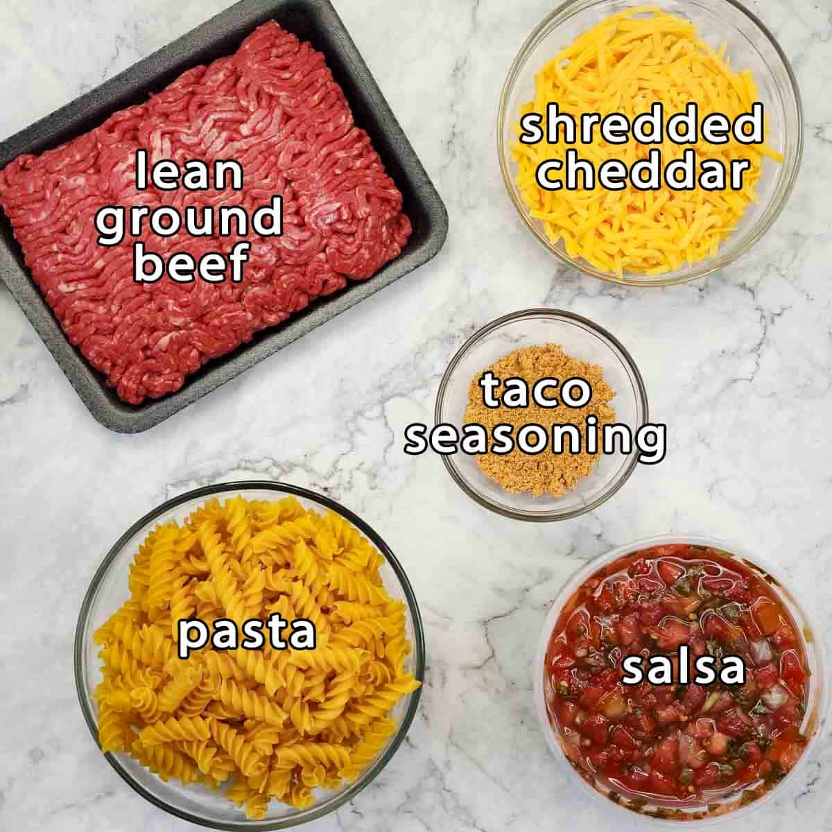 Overhead shot of ingredients - lean ground beef, shredded cheddar, pasta, salsa, and taco seasoning.