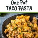 Side angled shot of taco pasta on a black plate garnished with fresh herbs with more herbs in the background.