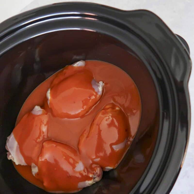 Overhead view of process shot 1 - place chicken in slow cooker and pour buffalo sauce over the chicken. Cover and cook for 6-8 hours on low.