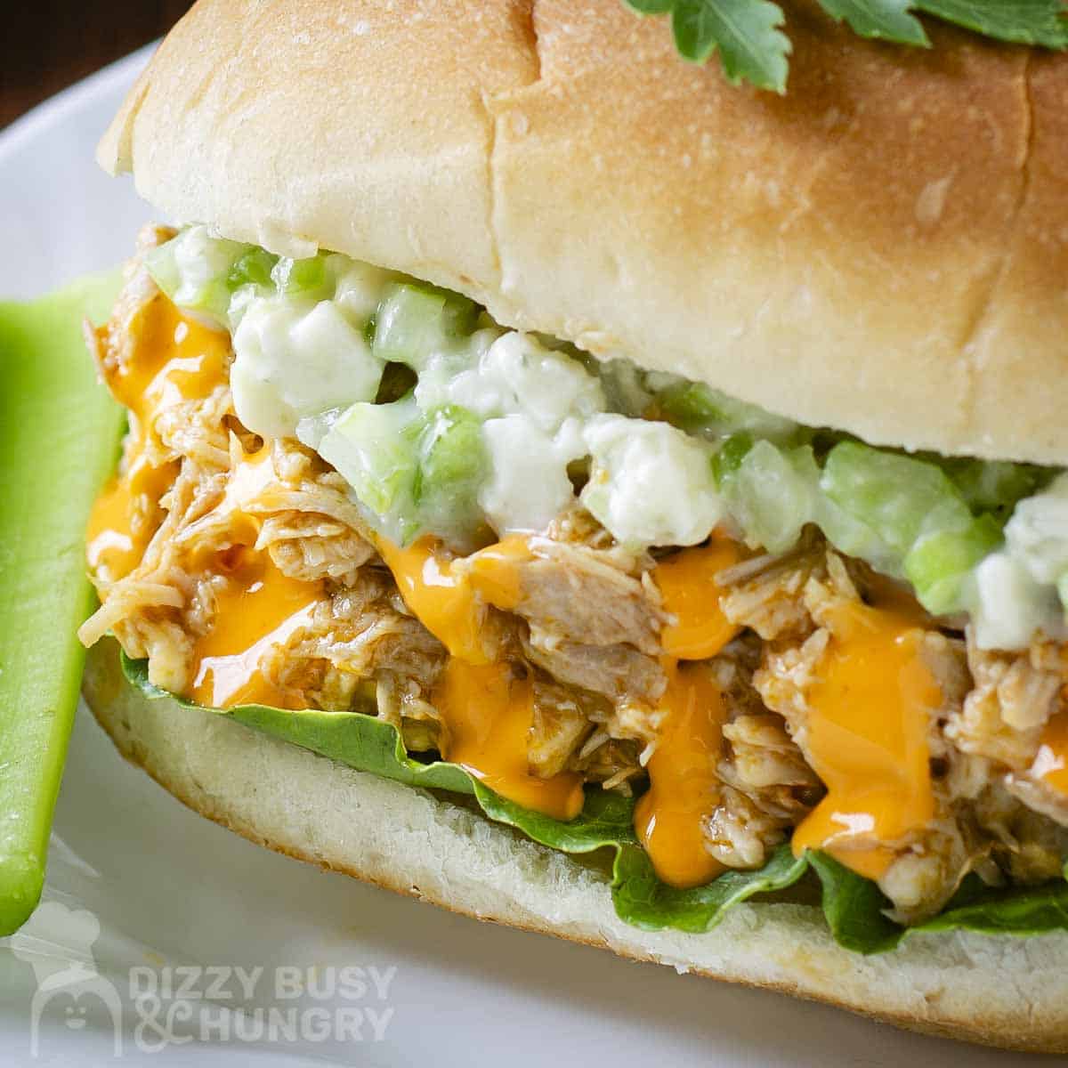 Side close up shot of buffalo chicken sandwiches garnished with fresh herbs with a celery stick on the side on a white plate.