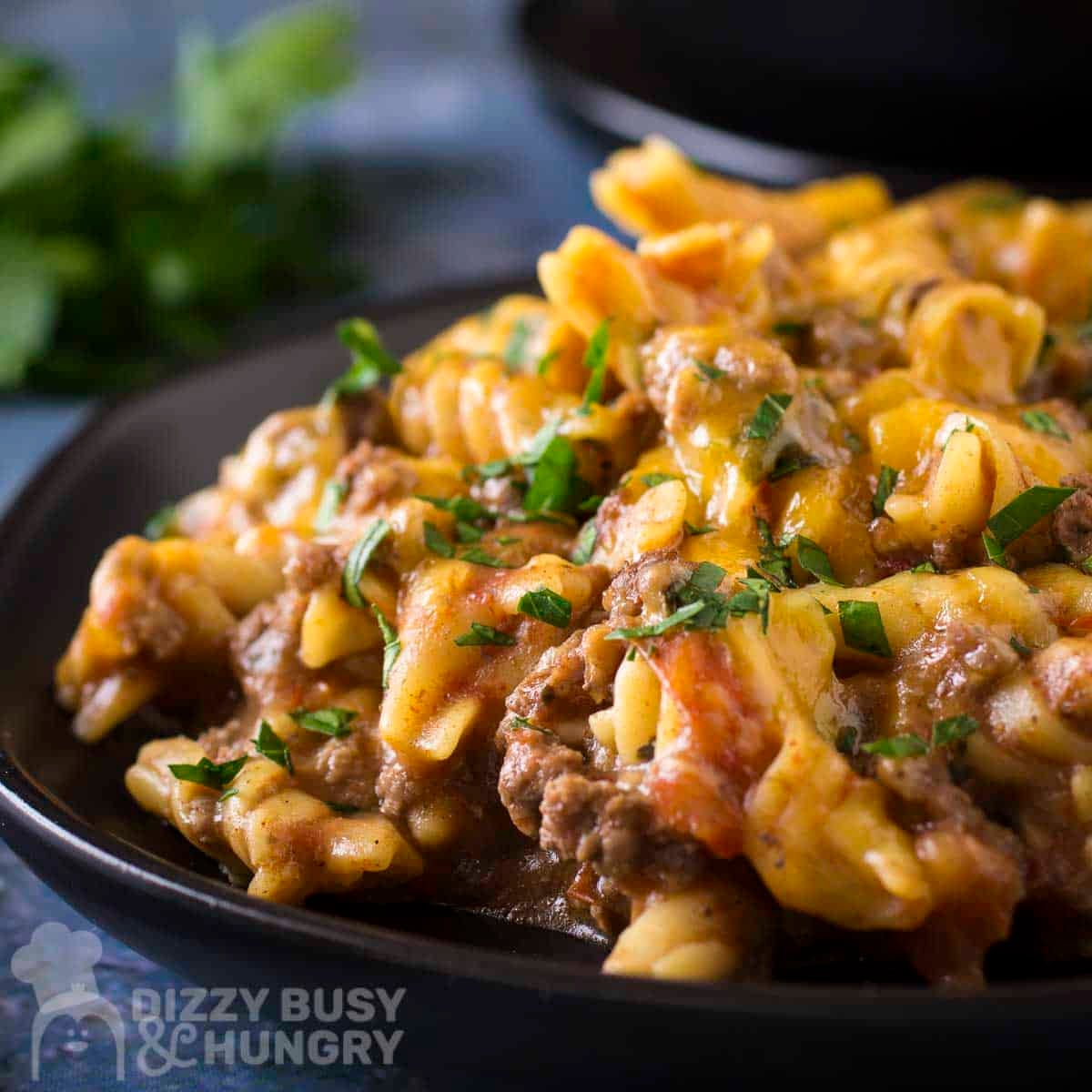 Side close up shot of taco pasta on a black plate garnished with fresh herbs with more herbs in the background.