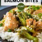 Side close up shot of teriyaki salmon and broccoli on a bed or rice garnished with fresh green onions on a black plate.