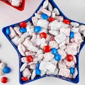Overhead shot of patriotic muddy buddies in a blue star bowl with more M&Ms on the side.