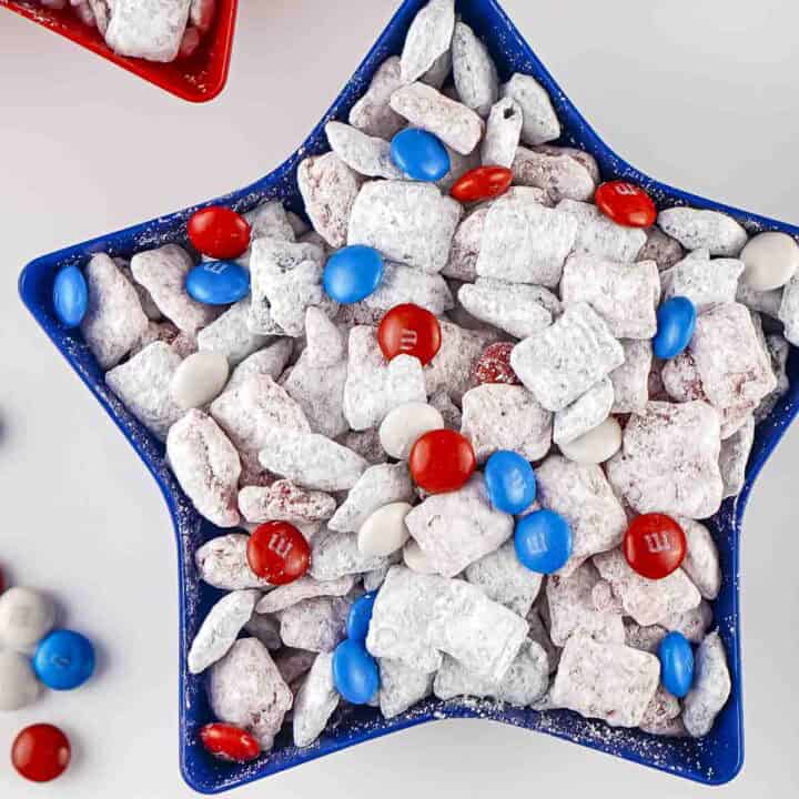 Overhead shot of patriotic muddy buddies in a blue star bowl with more M&Ms on the side.